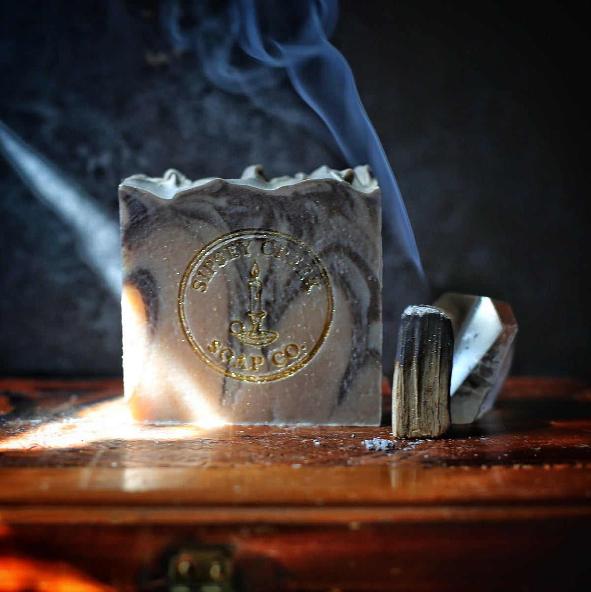 Palo Santo & Vanilla soap with gray and cream swirls and a gold Sipsey Creek stamp, beside an empty glass bottle and palo santo smudge stick.