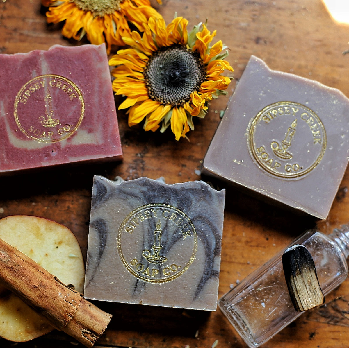 Three Hearth & Hollow soap bars with gold Sipsey Creek stamps, on wood beside sunflowers, apple slices, and a cinnamon stick.