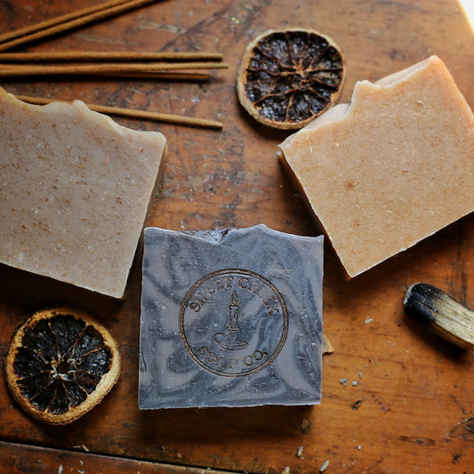 Three Apothecary Collection soap bars in orange, peach, and taupe with textured tops, arranged on draped cream fabric.
