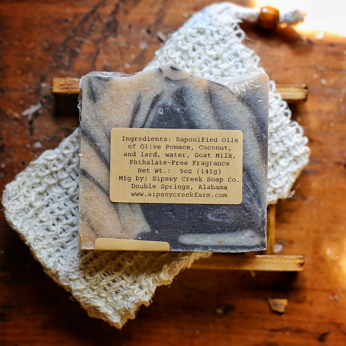 Back of wrapped Papa’s Pipe soap showing its ingredient and 5-ounce weight label, on a knitted cloth over a wooden soap dish.