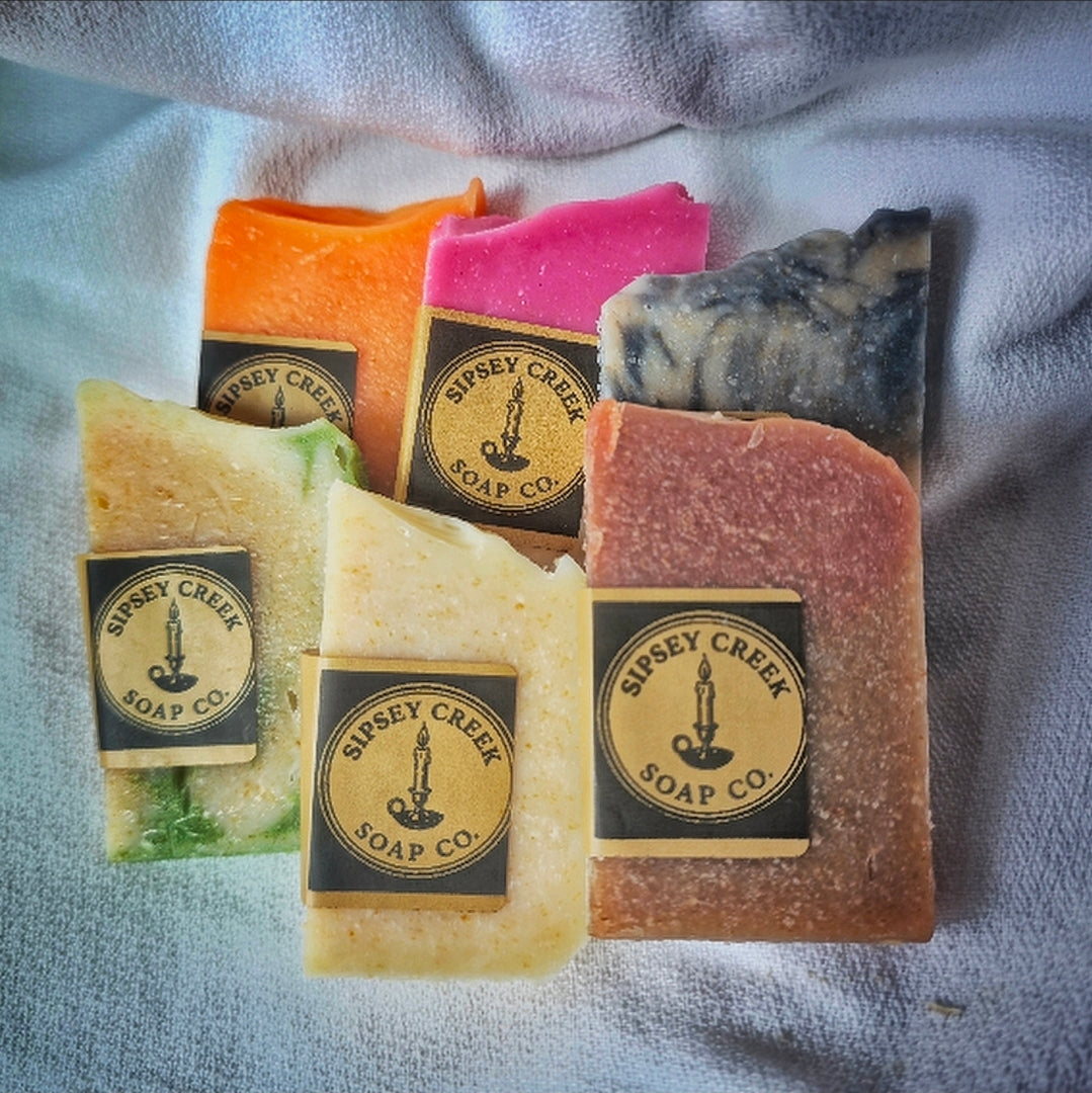 Six colorful Sipsey Creek sample soap bars arranged on a light towel, with black and gold logo labels on five bars