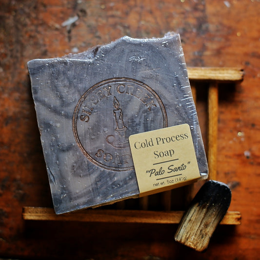 Wrapped gray marbled Palo Santo soap with a Sipsey Creek stamp and front label, on a wooden dish beside a charred wood stick