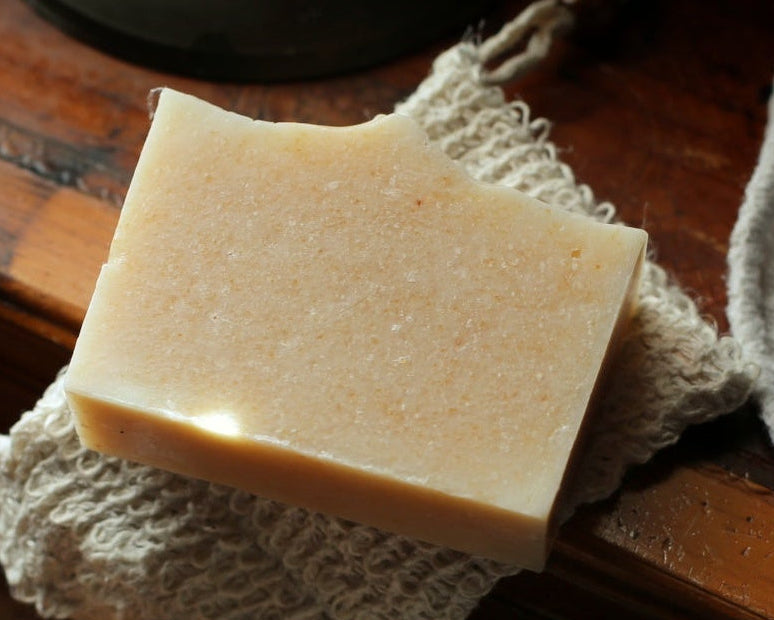 A rectangular bar of pale beige soap resting on a textured off-white cloth over a dark wooden surface.