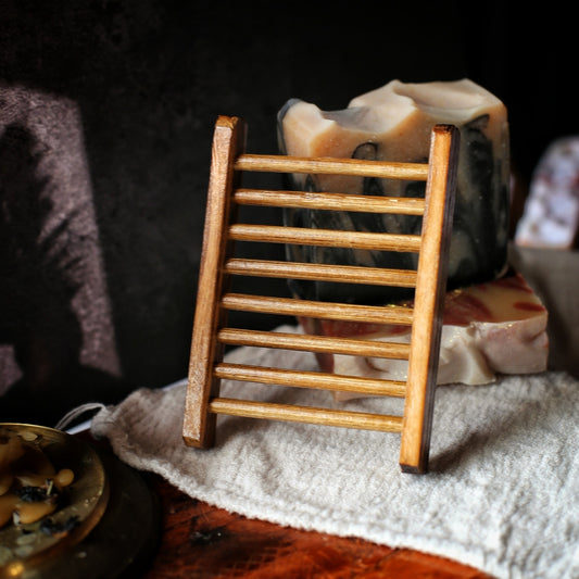 A  wooden soap tray standing upright on a white towel next to a brass dish, with a unwrapped bar of soap in the background.